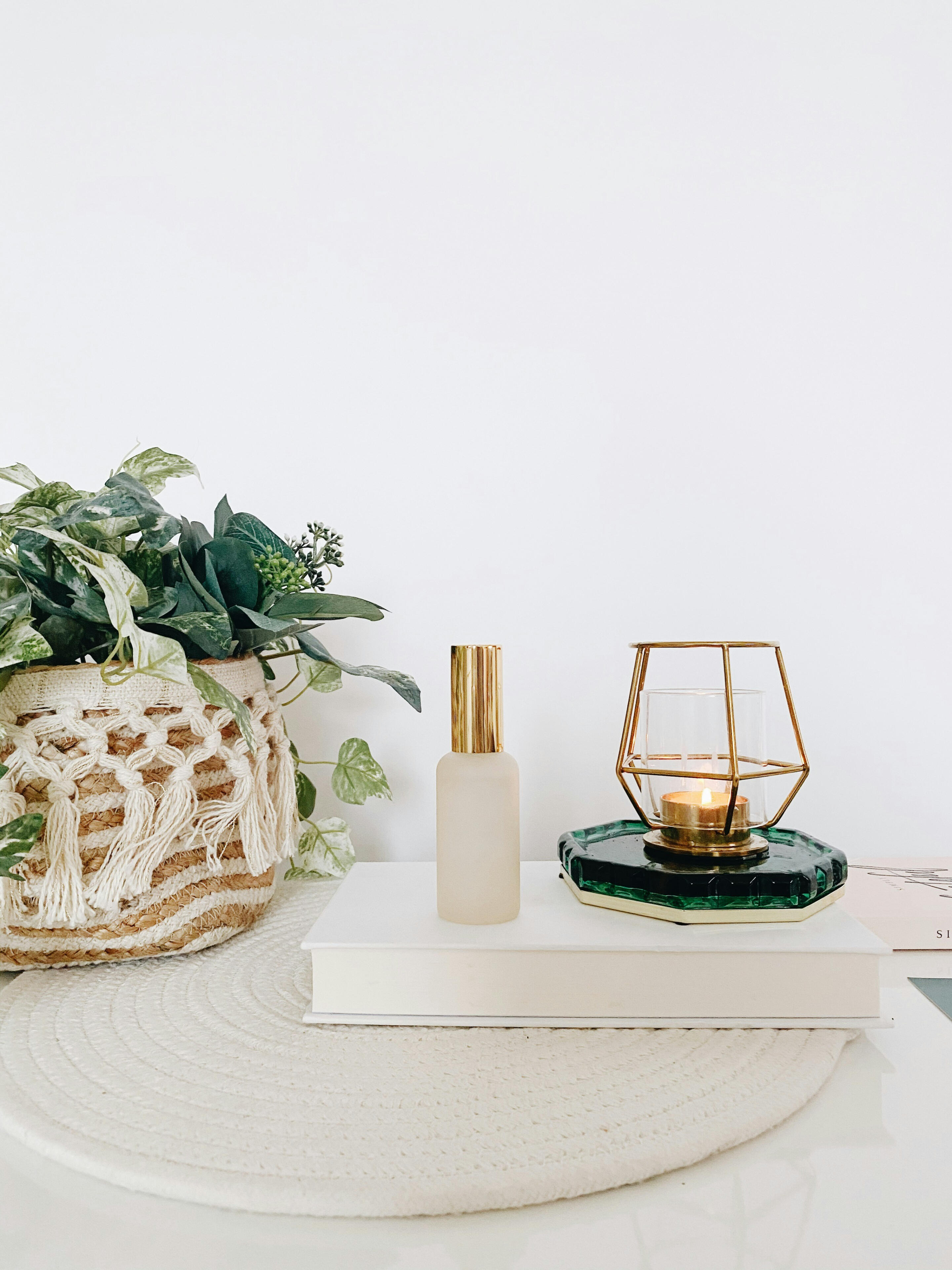 A candle, plant in a boho basket, neutral spray bottle and a book