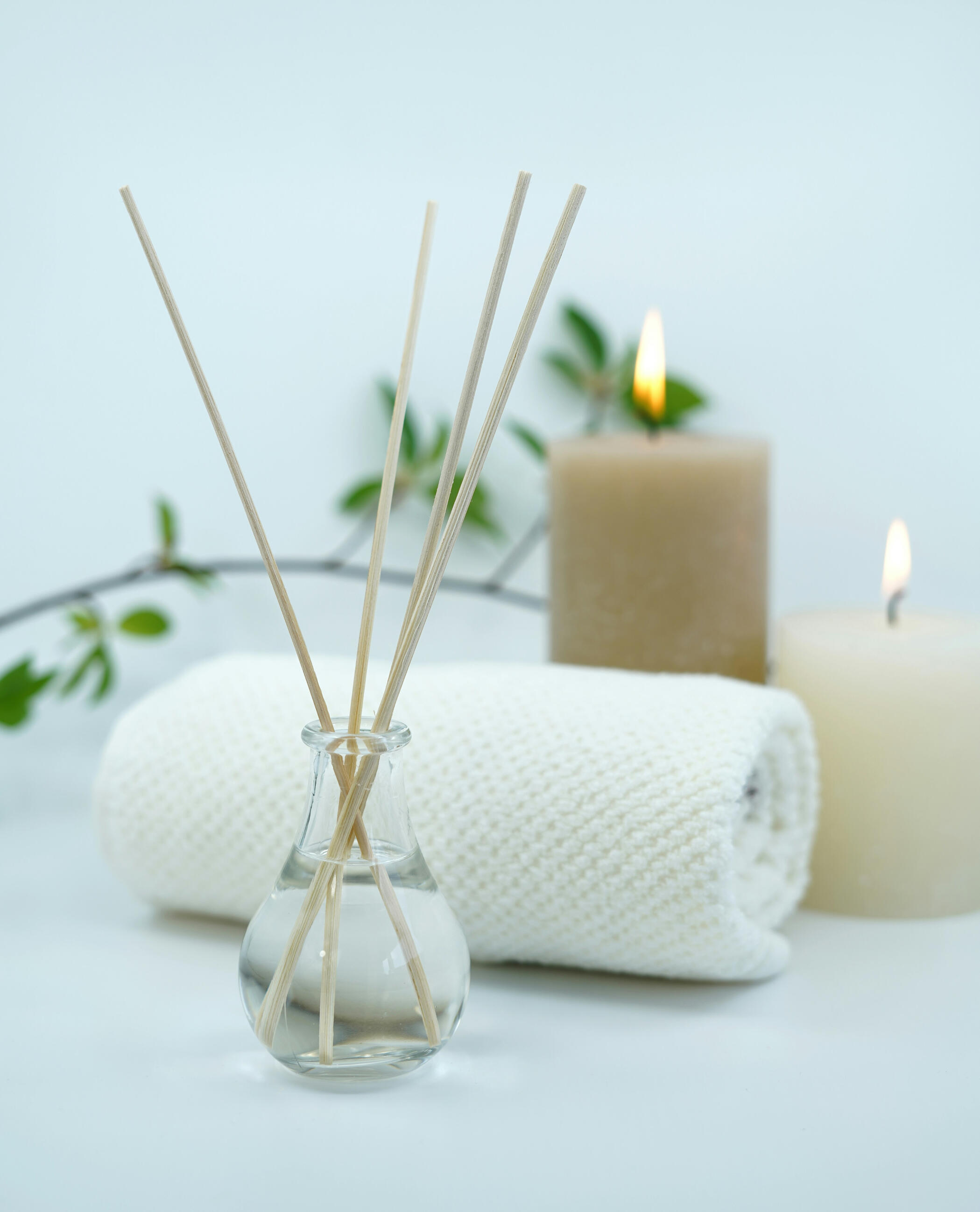 A spa-like scene with a diffuser, a rolled towel, candles and a plant